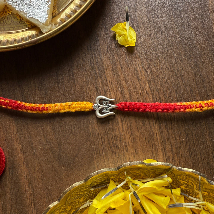 Two colorful threads with a silver clasp on a wooden surface, one next to a plate of cookies and the other next to a bowl of yellow flowers.